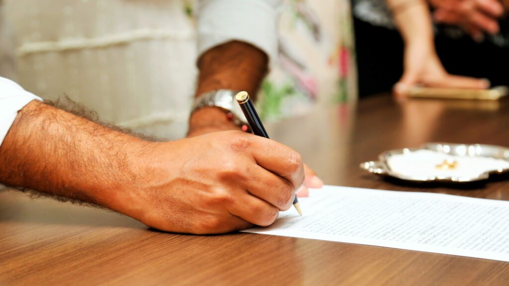 Close-up of a person signing a legal document, illustrating the Power of Attorney execution process for an NRI property sale